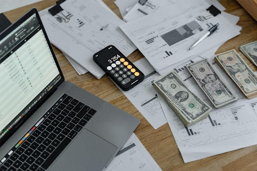 Table with laptop, calculator, money, financial documents.